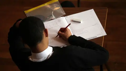 PA Media A student holds a pencil as they sit a maths exam