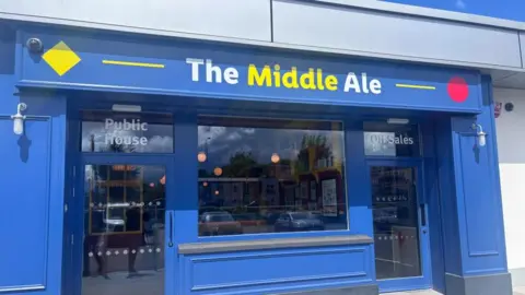 The front of a pub called the Middle Ale. It is owned by Lidl and shares its colour scheme of blue, yellow and red.
