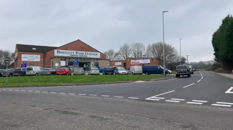 The spur road which has undergone improvements. The road runs alongside Bartlett Park Garage and looks to be newly resurfaced.