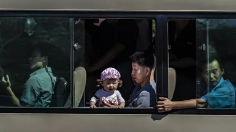 Tariq Zaidi Baby looking out of a Pyongyang bus while her father holds her secure