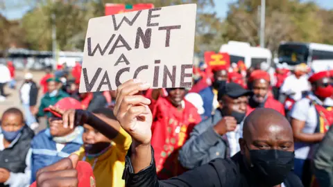 AFP An EFF supporter holds up a sign saying: "We want a vaccine" in Pretoria, South Africa - Friday 25 June 2021