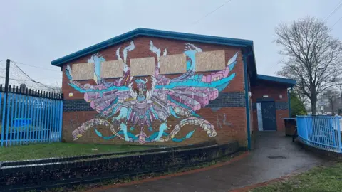 BBC a boarded up building with a mural and graffiti on it