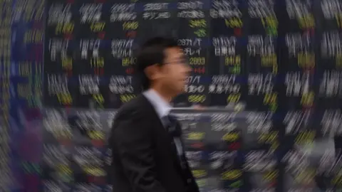 Getty Images Man walking past stock boards in Tokyo