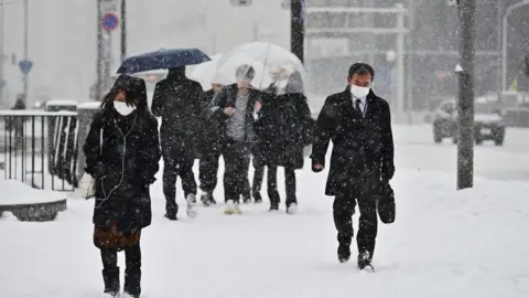 Getty Images People in Hokkaido wear masks and walk through snowfall (Feb 2020)