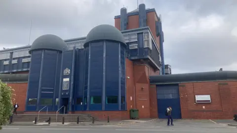 The outside of HMP Birmingham - a red brick building with blue exterior panneling.