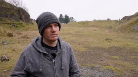 George Linnane is photographed above ground when he returned to Ogof Ffynnon Ddu nature reserve, in the Brecon Beacons. He is wearing a grey hoodie and grey beanie hat. He is looking away from the camera.