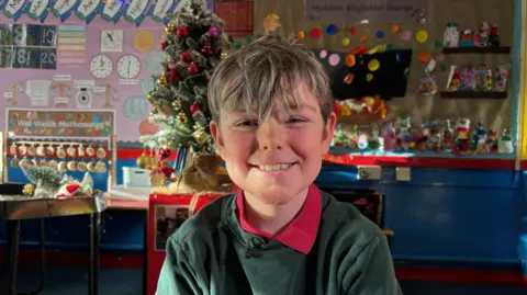 BBC Efan smiles. His hair is ruffled and he is wearing a green jumper  