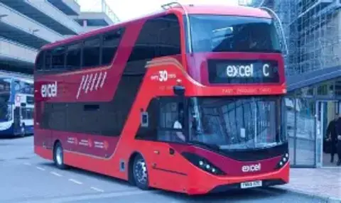 First Bus Pictured is a large red double-decker bus. It has the words "excel C" in its front window. On the side is a list of the locations that it stops at. 