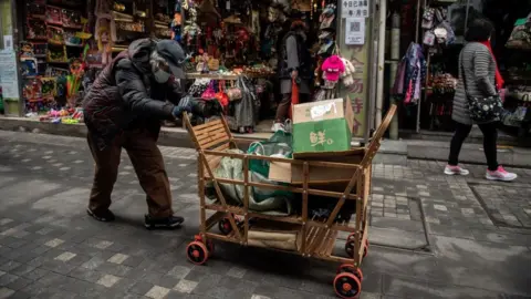 Getty Images An elderly woman pushes a cart after searching through rubbish bins to collect recyclable items to sell, along a street near the Great Hall of the People in Beijing.