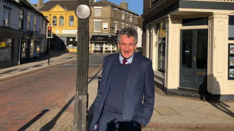 Vikki Irwin/BBC Peter Prinsley standing in the market square in Stowmarket. He is wearing a blue suit. He has grey and dark hair and is wearing glasses