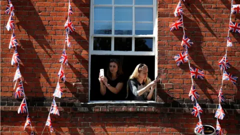 Reuters Women take photos on their smartphones as they lean out of the window of a building near Windsor Castle