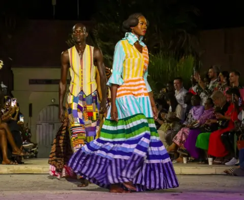 Getty Images Models wearing colourful clothing walking the runway.
