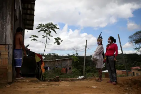 Reuters Vanderlecia and Natalina wear protective masks as they talk to a neighbour outside of his home