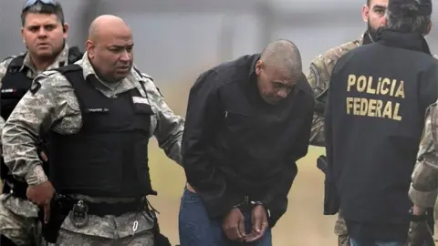 Reuters Federal Police agents escort Adelio Bispo de Oliveira, suspected of stabbing Brazilian presidential candidate Jair Bolsonaro, to transfer him to a federal prison in Campo Grande, Mato Grosso state, at Francisco Alvares de Assis airport in Juiz de Fora, Brazil, September 8, 2018.