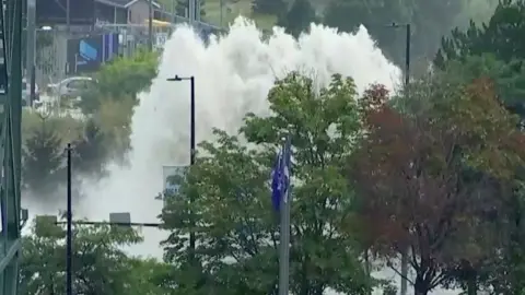  A giant plume of water erupts above the tree line and street lights