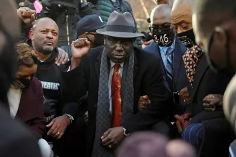 Nicholas Pfosi / Reuters Attorney Ben Crump, Reverend Al Sharpton and the Floyd family kneel following a news conference outside the Hennepin County Government Center, on 29 March 2021