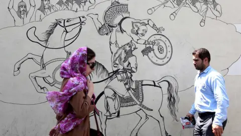 AFP People walk past a mural in Tehran, Iran (25 June 2019)