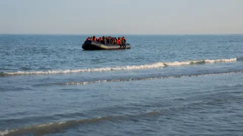 A small boat with migrants onboard wearing orange life jackets.