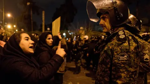 MONA HOOBEHFEKR/ISNA/AFP via GETTY IMAGES A woman talks to a policeman at a gathering in front of Amirkabir University in Tehran