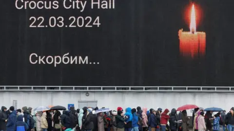 Reuters People queue to lay flowers at a makeshift memorial to the victims of a shooting attack set up outside the Crocus City Hall concert venue in the Moscow Region, Russia, March 24, 2024.