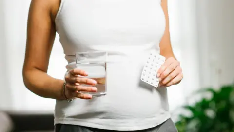 Getty Images Pregnant woman holding pack of folic acid tablets and a glass of water