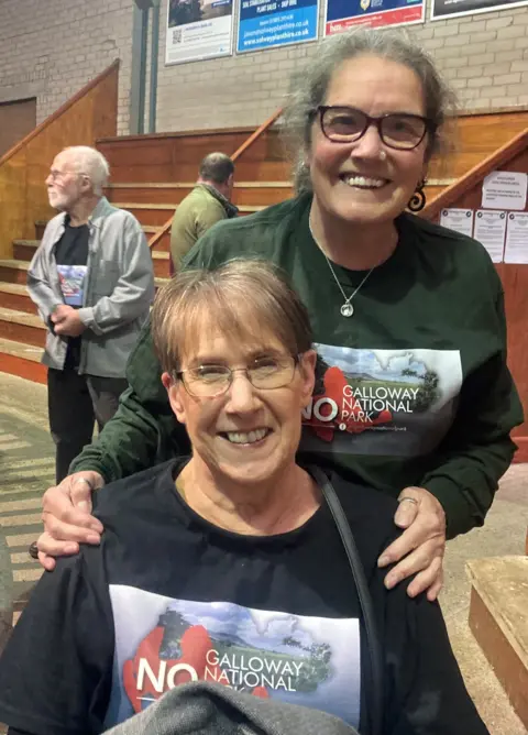 No Galloway National Park Two women - one seated and one standing - both wearing glasses and No to the Galloway National Park jumpers