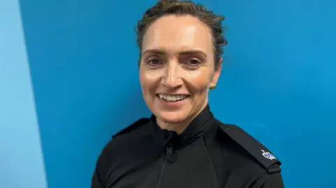 A photo of Supt Mairi MacInnes. She is looking straight at the camera wearing a black police uniform shirt with epilets. She has short brown hair.
