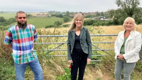 BBC Gavin Heathcote (left), Cllr Sarah Bevan (centre) and Cllr Karen Walker (right) next to the Greenlands Road development site in Peasedown St John