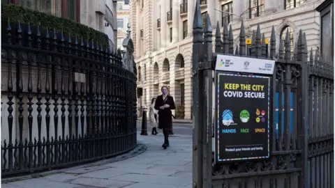 PA Media A person in a mask walks past a 'Keep the City Covid secure' sign