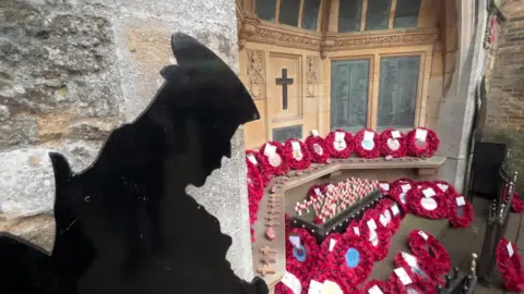 Silhouette of soldier with head bowed and circle of wreaths on a war memorial