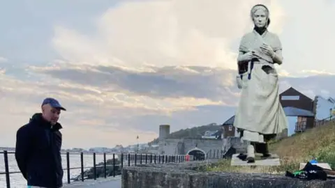 Mary Anning Rocks Model of Mary Anning statue superimposed on a photo of the location next to a footpath beside the sea