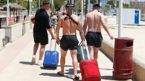 Reuters Tourists carrying luggage at Magaluf, after the UK eased travel restrictions to Mallorca