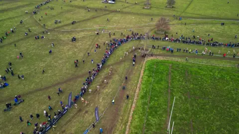 Ben Cuthbertson An aerial photo of the course which is made up entirely of grass with brown patches where the ground has been ran on. The course curves across the field and is marked by white tape. Spectators are by the side of the course.