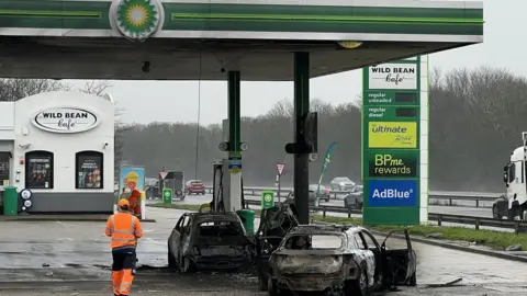 Richad Knights/BBC The burnt out shells of two cars on a petrol forecourt