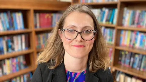 Headteacher Louise Cowley in front of book shelves in the library