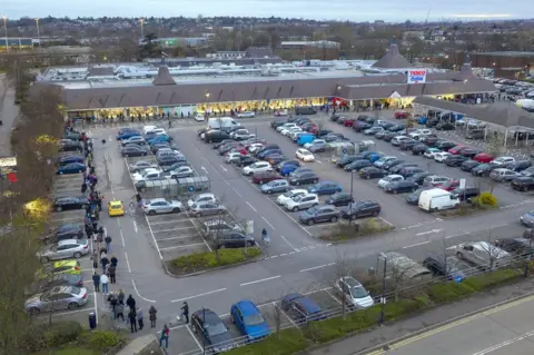 Chris Gorman / Big Ladder A large supermarket with a very long queue winding around the car park