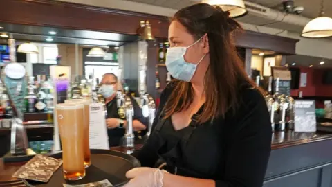 PA Media A waitress wearing a face mask carrying a tray holding two pints of beer