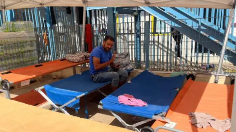 A man sitting on a camping bed waves