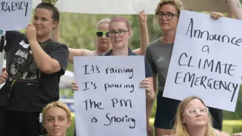 EPA People hold placards critical of Scott Morrison - one accuses him of "snoring" and another says "announce a climate emergency"