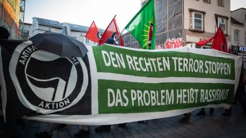 Getty Images Flags are raised above an anti-fascist demonstration, behind a banner reading, in German, "Stop the far-right terror, the problem is called racism"