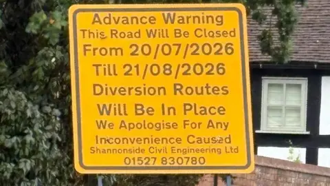 A yellow roadworks sign describes the closure from 20 July to 21 August, with an apology and contact number for the firm carrying out the works.