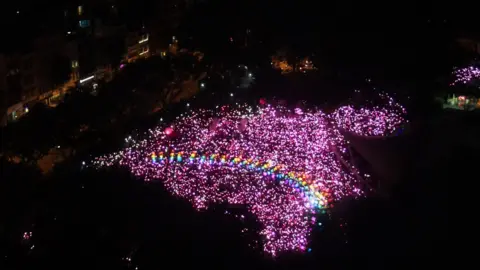 Pink Dot An aerial photo of the demonstration space in Singapore, filled with hundreds of pink lights in an irregular shape. Arcing across the centre is a series of coloured lights creating the image of a rainbow, a well-known LGBT symbol.