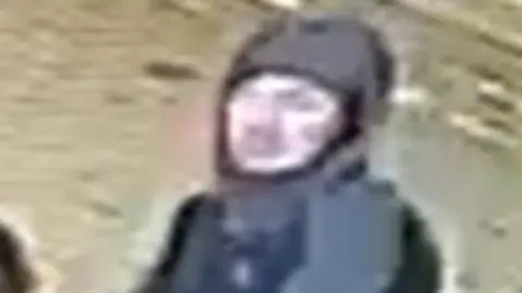 Blurred CCTV image of a man in a dark hooded coat