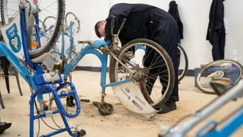 Joe Giddens/PA Media Man works on a bike which is upside down. Other bikes are visible.