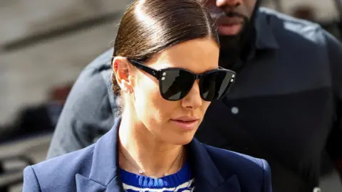 Reuters Rebekah Vardy arrives at court on Thursday, alongside her security guard, wearing a blue and white patterned dress under a blue blazer