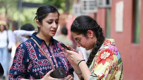 Students check their results on mobile phones after the declaration of the CBSE Class XII results at the premises of St. Thomas' School on May 13, 2026 in New Delhi, India.