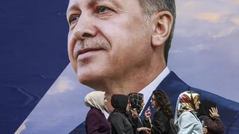 EPA Women walk in front of an election campaign poster of Turkish President Recep Tayyip Erdogan in Istanbul