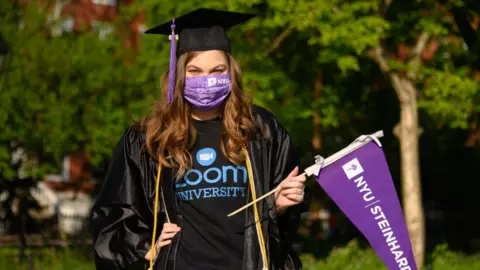 Getty Images A student wears a protective face mask, graduation cap and graduation gown in Washington Square Park during the coronavirus pandemic on May 15, 2020