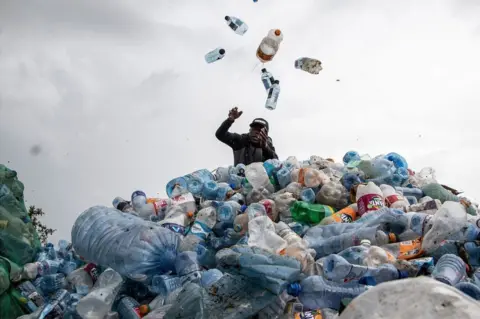 JAMES WAKIBIA/GETTY IMAGES James Githae, the Chairman of Nakuru County Waste Pickers Association, sorts plastic bottles at Gioto dumping site.