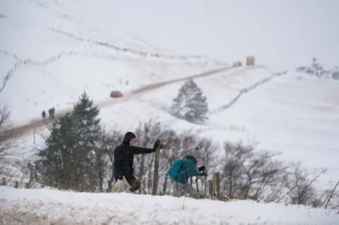 Jacob King/PA Media Walkers cross field covered in snow by the A53 close to Buxton in Derbyshire, amid freezing conditions in the aftermath of Storm Arwen